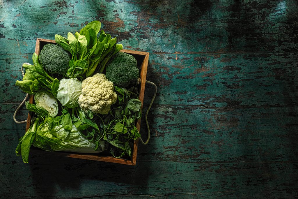 Vegetais de folhas verdes frescas em um caixote de madeira antigo sobre uma mesa de madeira antiga de turquesa.